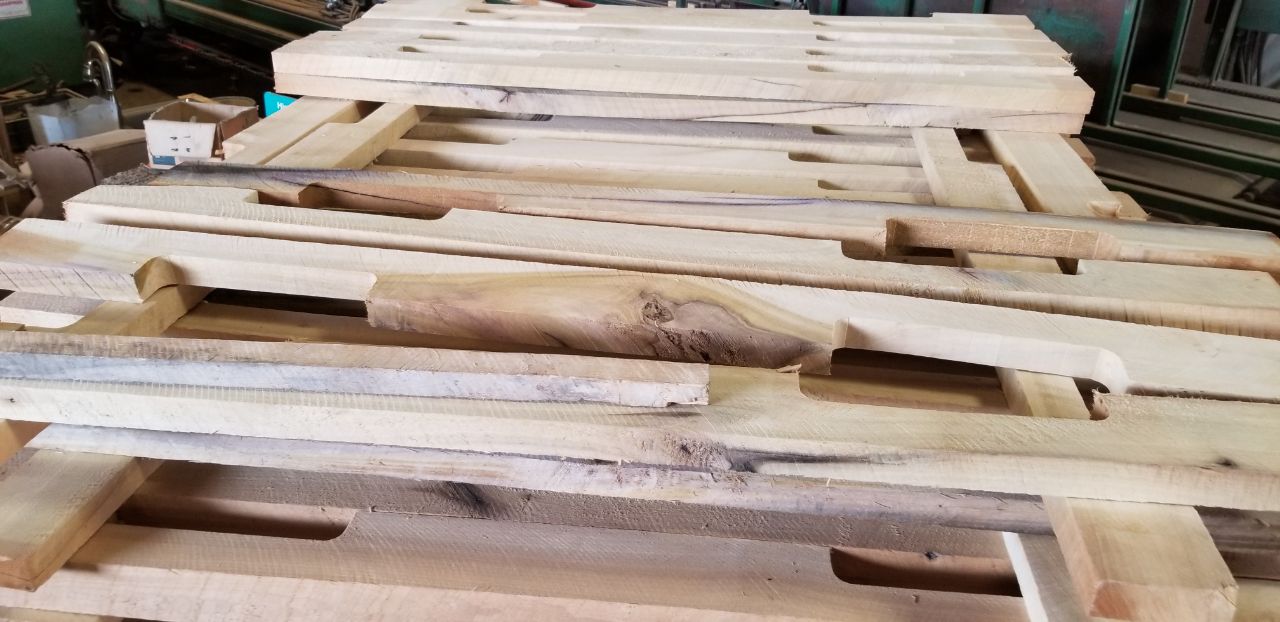 Shaped and notched wood components stacked beside workshop machinery